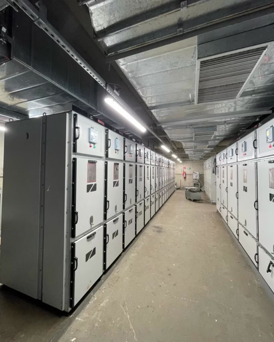 Sala elétrica industrial com linha de cubículos de média tensão e leitos de cabos no teto