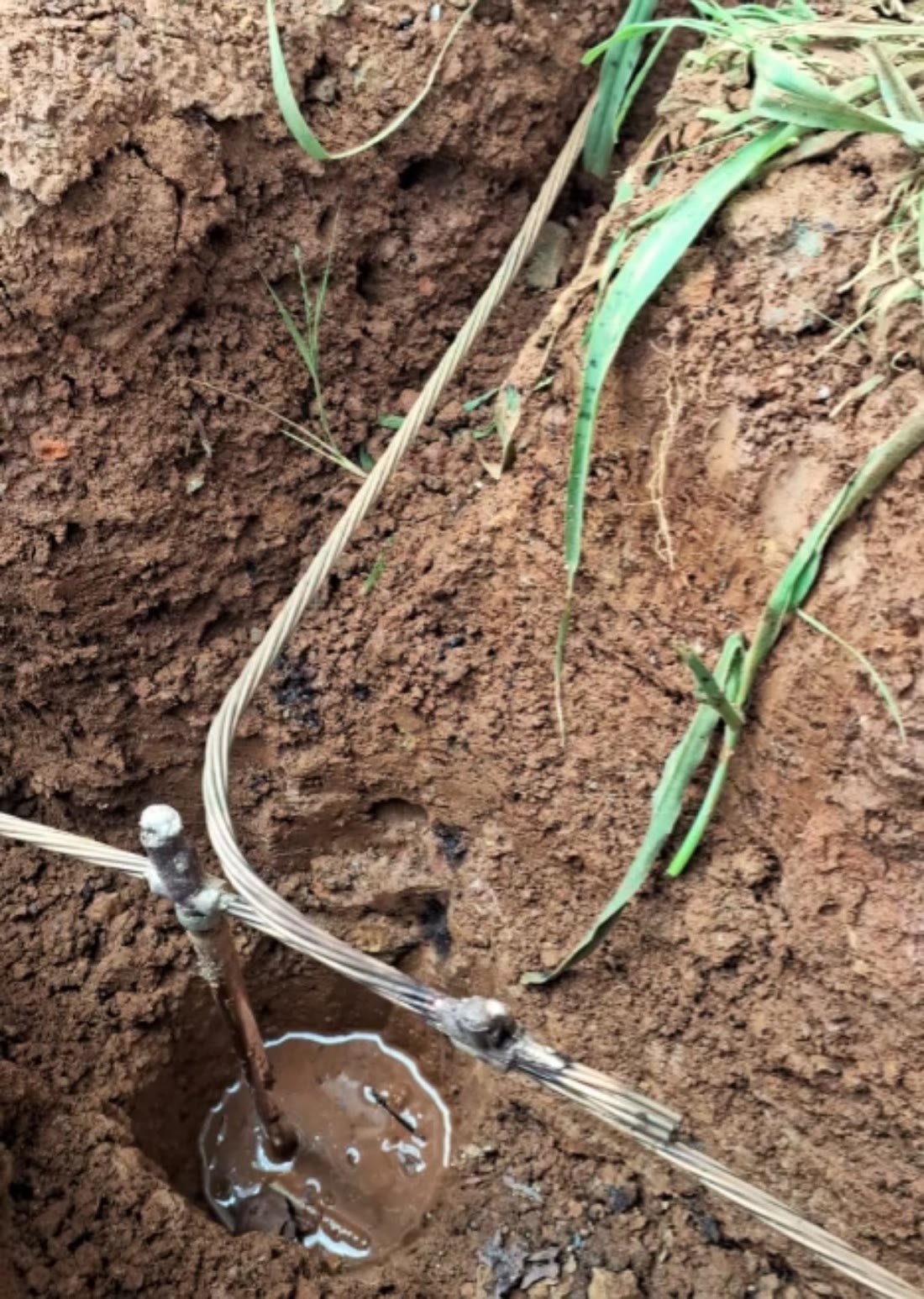 Cabo de aterramento de cobre sendo conectado a haste enterrada no solo